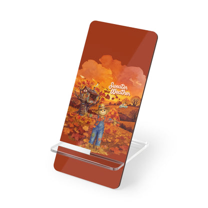 A rectangular acrylic PHONE STAND with rounded corners, shown on a clear acrylic stand against a white background. The plaque features a printed autumn illustration with a scarecrow, orange and yellow leaves, a house, and the text 'Sweeter Weather'.