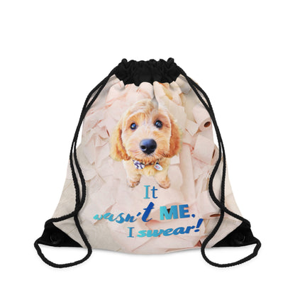 A drawstring gym bag with a printed graphic of a golden-brown puppy and the text 'It wasn't ME. I swear!' on a light beige background, with black drawstring cords.