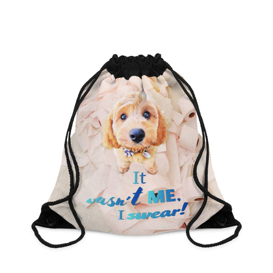 A drawstring gym bag with a printed graphic of a golden-brown puppy and the text 'It wasn't ME. I swear!' on a light beige background, with black drawstring cords.