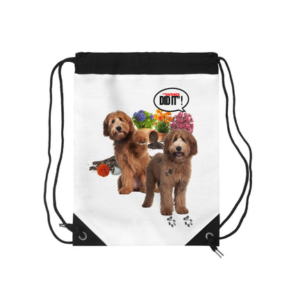 A white drawstring bag with black cords and black corner panels, featuring a printed graphic of two brown dogs, colorful flowers, and a speech bubble that says 'I DID IT!'.