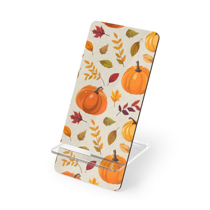 A phone stand with a fall autumn pattern featuring pumpkins and leaves on a cream background, supported by a clear acrylic base on a white studio background.