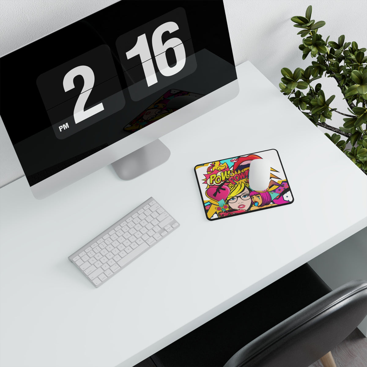 A colorful computer mouse pad with a vibrant pop-art illustration of a woman and the text 'POW POW' sits on a white desk next to a white mouse, keyboard, and monitor, with a green plant in the background.