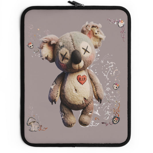 A laptop sleeve featuring a graphic print of a creepy, stitched teddy bear with a red heart on its chest, set against a dusty purple background with small skull and floral doodles. The sleeve has a black border and a black zipper on the left side.
