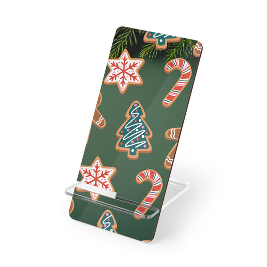 A slim rectangular phone stand with a dark green Christmas-themed pattern featuring gingerbread cookies, candy canes, and pine branches, shown on a clear acrylic stand against a white background.