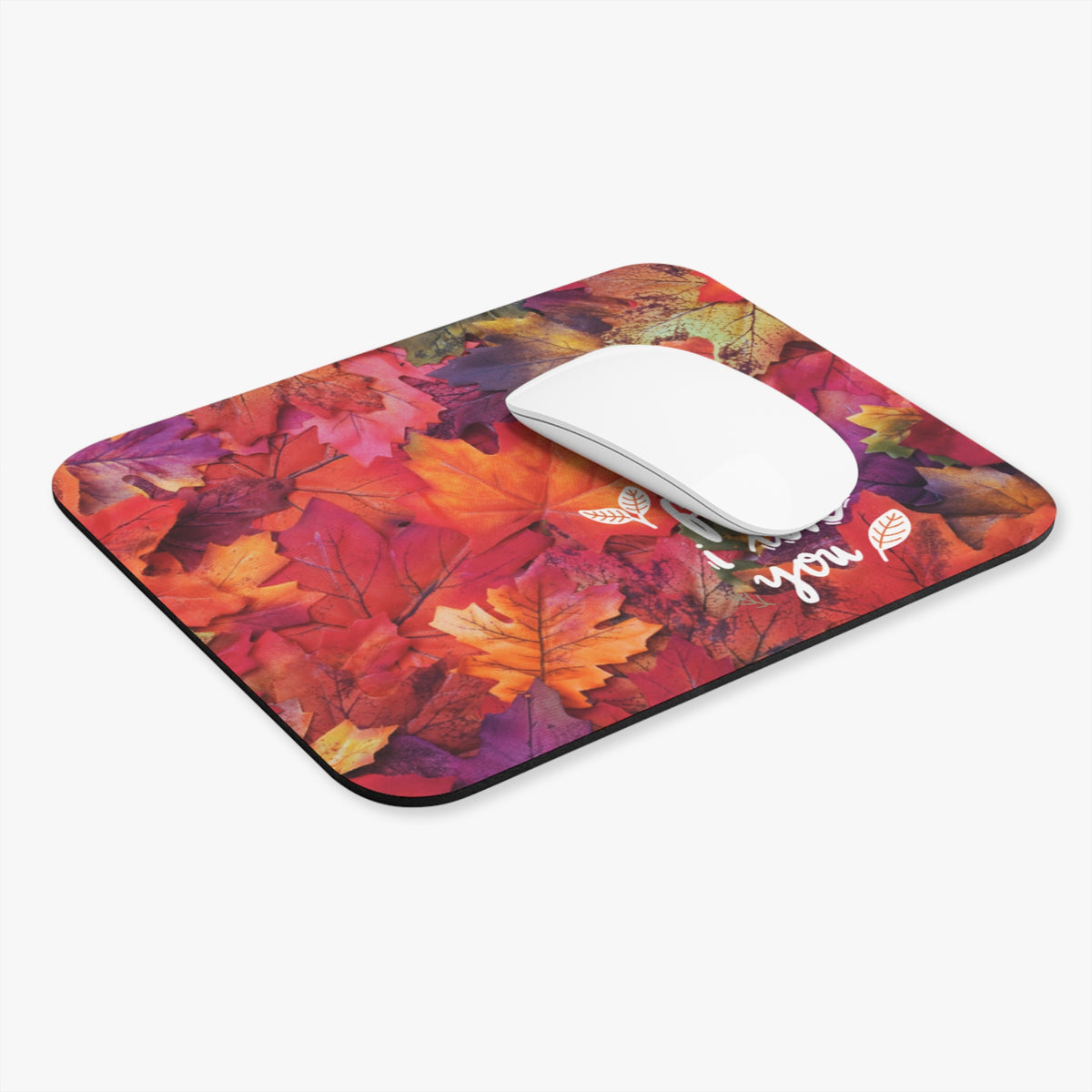 A rectangular computer mouse pad with a colorful autumn leaf pattern, featuring a white computer mouse on top, set against a plain light gray background.