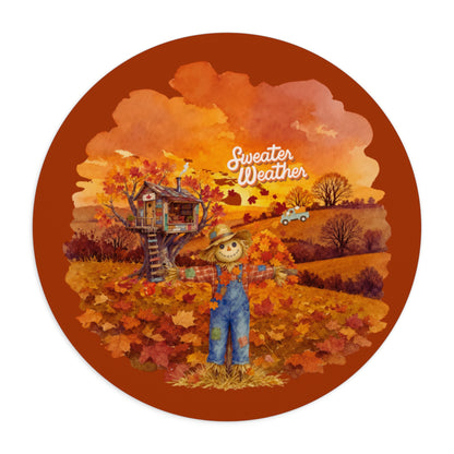A circular autumn-themed sticker or graphic featuring a scarecrow in blue overalls standing in a field of orange and red leaves, with a treehouse, hills, and the words 'Sweater Weather' on a rust-orange background.