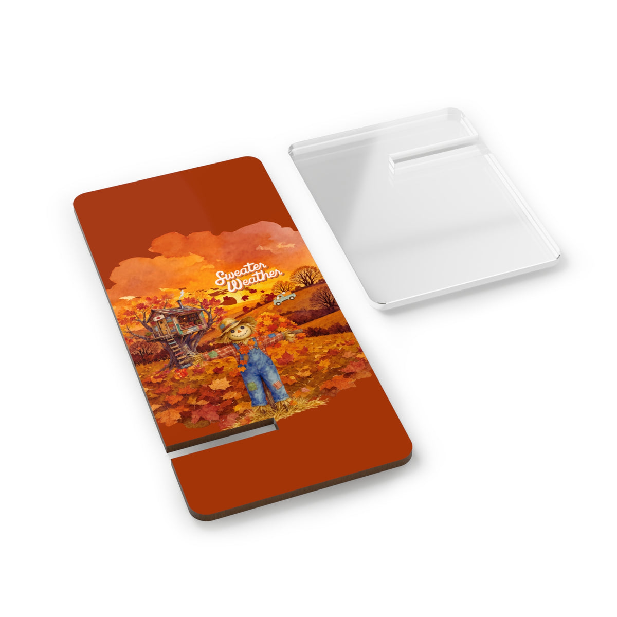 A rectangular PHONE STAND with a printed autumn illustration on the front, shown next to its clear plastic protective cover on a white background. The illustration features a scarecrow in blue overalls standing in an orange and yellow field with the text 'Sweeten Everything'.