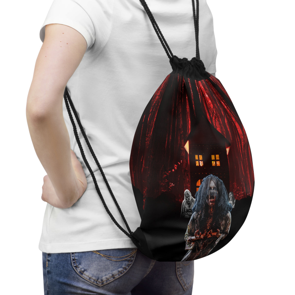 A person wearing a white t-shirt and blue jeans carries a black drawstring backpack with a spooky Halloween graphic of a haunted house and a zombie.