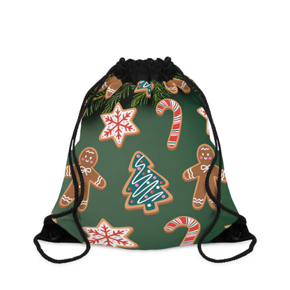 A drawstring backpack with a dark green background and a festive holiday print featuring gingerbread cookies, candy canes, snowflakes, pine branches, and a Christmas tree. The drawstrings are black.