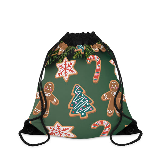 A drawstring backpack with a dark green background and a festive holiday print featuring gingerbread cookies, candy canes, snowflakes, pine branches, and a Christmas tree. The drawstrings are black.