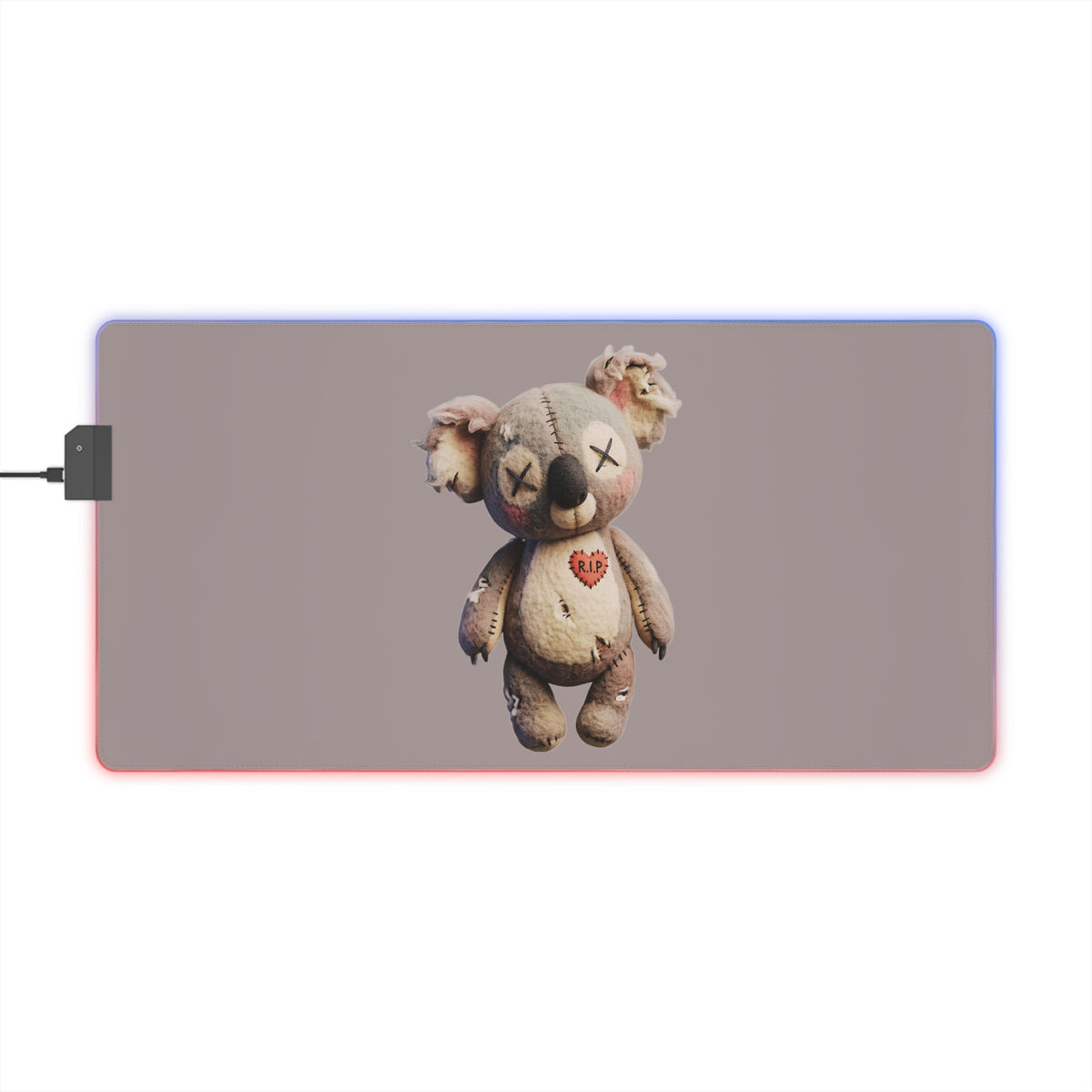 A rectangular gaming mouse pad with rounded corners featuring a printed graphic of a distressed, stitched teddy bear with a small monkey on its head. The mouse pad is shown with RGB lighting glowing in red and blue, with a power cable connected on the left, set against a plain white background.