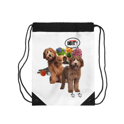 A white drawstring backpack with black top trim and black cords, featuring a printed graphic of two brown dogs, colorful flowers, a speech bubble that says 'I DID IT!', and black triangular corner accents.