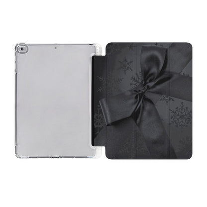 A clear protective case for a tablet shown next to its black folio-style back cover decorated with a dark gray ribbon bow and subtle snowflake pattern, on a plain white background.