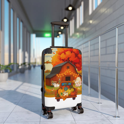 A hard-shell rolling suitcase with an autumn-themed printed design stands in a modern airport or terminal corridor. The suitcase features a colorful illustration of a barn, pumpkins, sheep, and a large orange tree, with a white lower section and black wheels and handle.