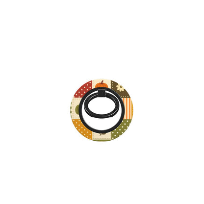 A circular phone grip stand featuring a fall-themed patchwork pattern with orange pumpkins, green polka dots, and cream stripes, with a black central ring.