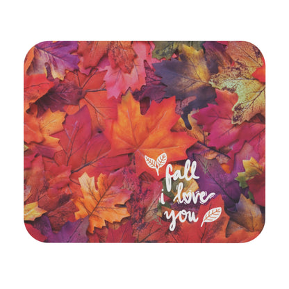 A square mouse pad with rounded corners featuring a colorful autumn leaf pattern in shades of orange, red, pink, and purple, with the white script text 'fall i love you' and small white leaf illustrations.