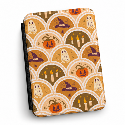 A KINDLE COMPATIBLE CASE featuring a repeating Halloween-themed scallop pattern with jack-o'-lanterns, ghosts, witch hats, and candles in orange, brown, cream, and purple tones, shown on a white background.