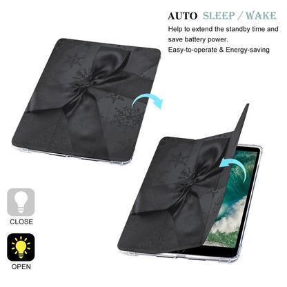 Black folio-style tablet case with a satin ribbon bow and subtle snowflake pattern, shown closed and open with a tablet inside on a white background. Text reads 'AUTO SLEEP / WAKE' and includes close/open instructions with light bulb icons.